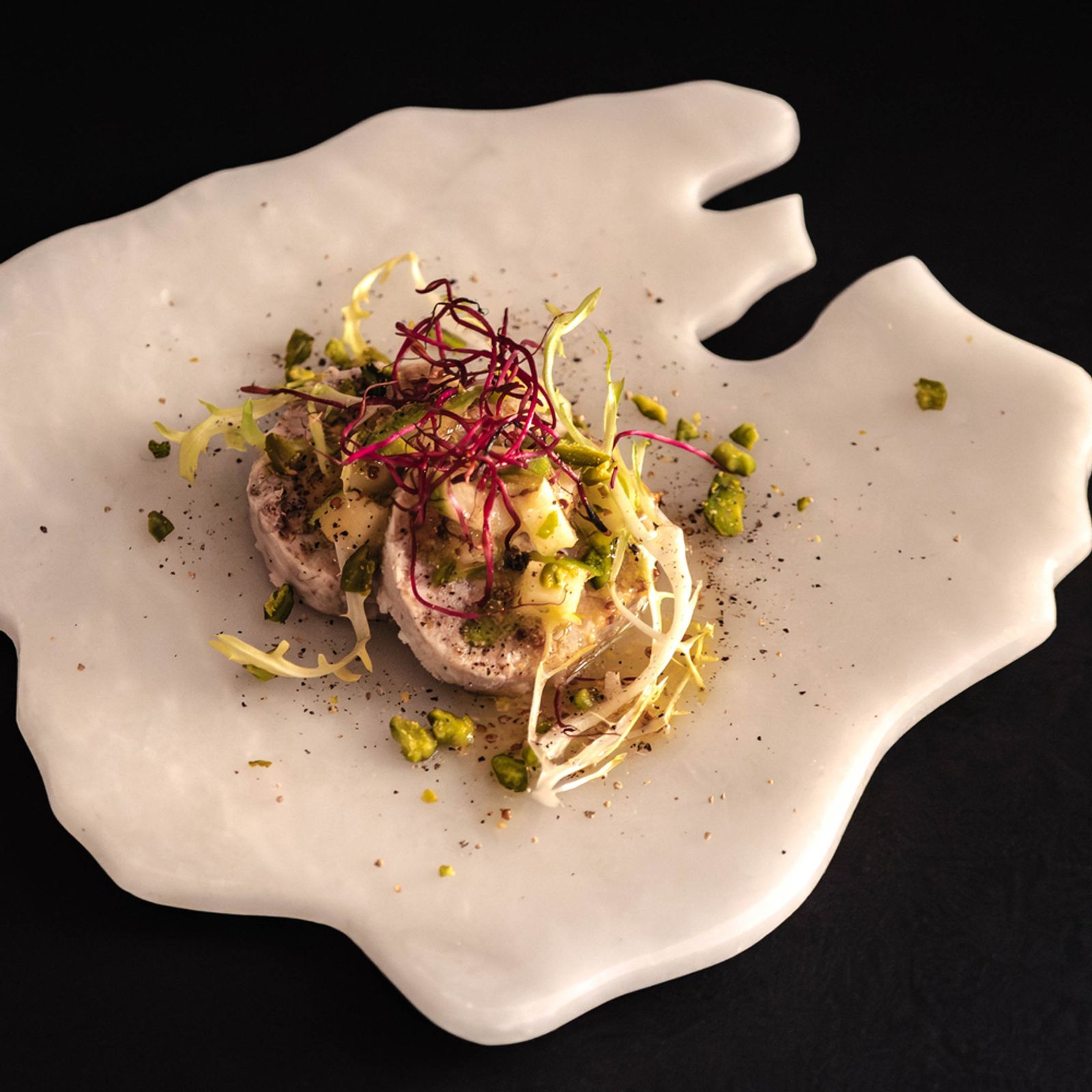 Ca'n Boqueta (Sóller): Bib Gourmand aan de Gran Via 6 Voorgerecht van Ca'n Boqueta met pistache en fijne kiemen, geserveerd op een onregelmatig gevormd licht bord