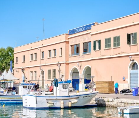 Ca n'Eduardo in Palma: visrestaurant boven de oude visafslag 9 De zalmroze gevel van restaurant Ca n'Eduardo boven de visafslag van Palma, met het uithangbord op het dak en vissersboten aan de kade