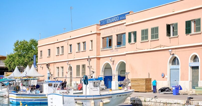 Ca n'Eduardo in Palma: visrestaurant boven de oude visafslag 1 De zalmroze gevel van restaurant Ca n'Eduardo boven de visafslag van Palma, met het uithangbord op het dak en vissersboten aan de kade