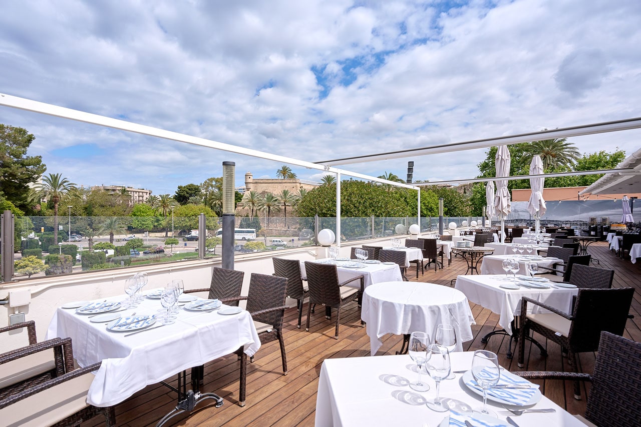 Het dakterras van Ca n'Eduardo in Palma met wit gedekte tafels, rieten stoelen en zonneschermen boven de haven