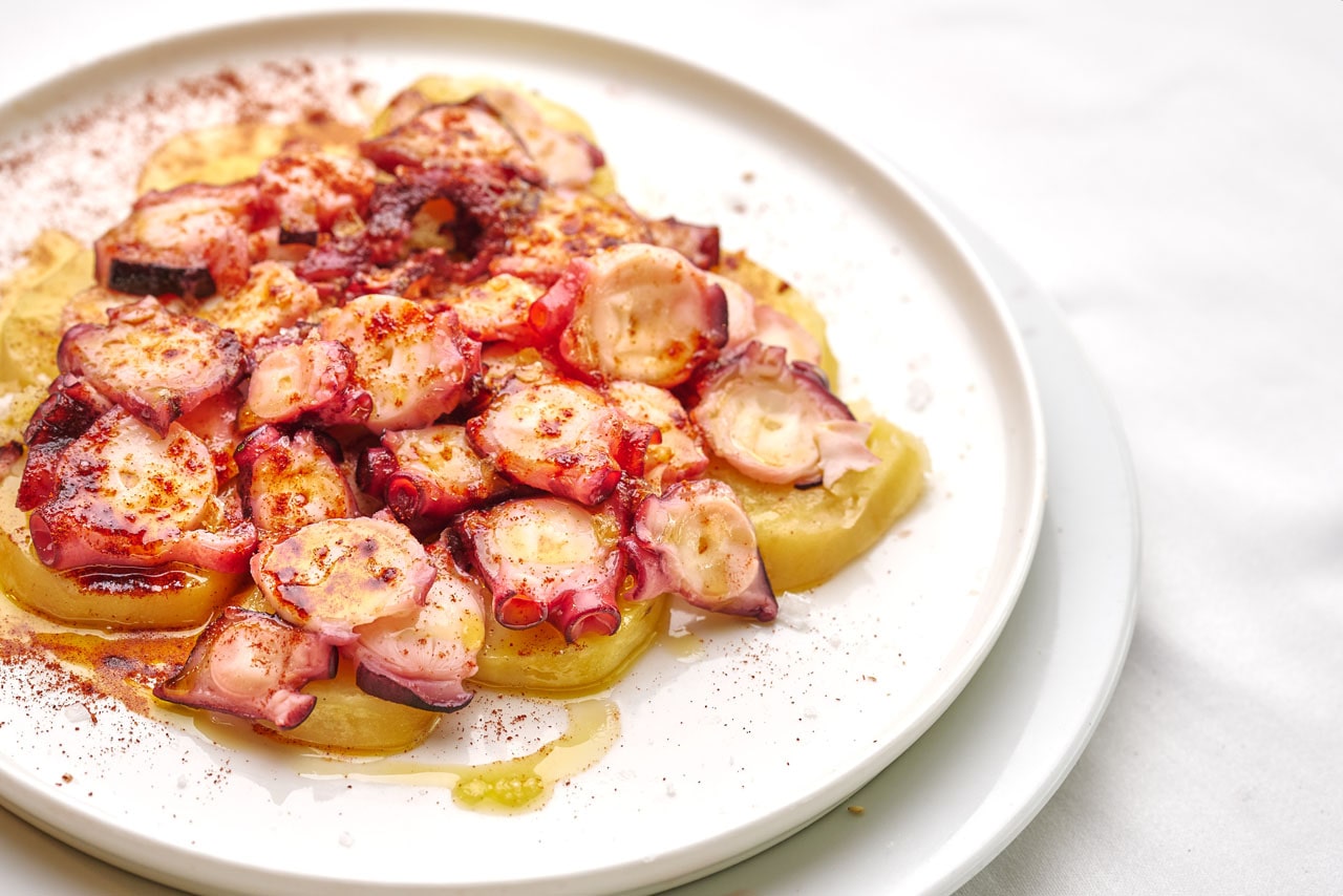 Pulpo a la gallega met schijfjes aardappel en paprikapoeder op een bord van Ca n'Eduardo
