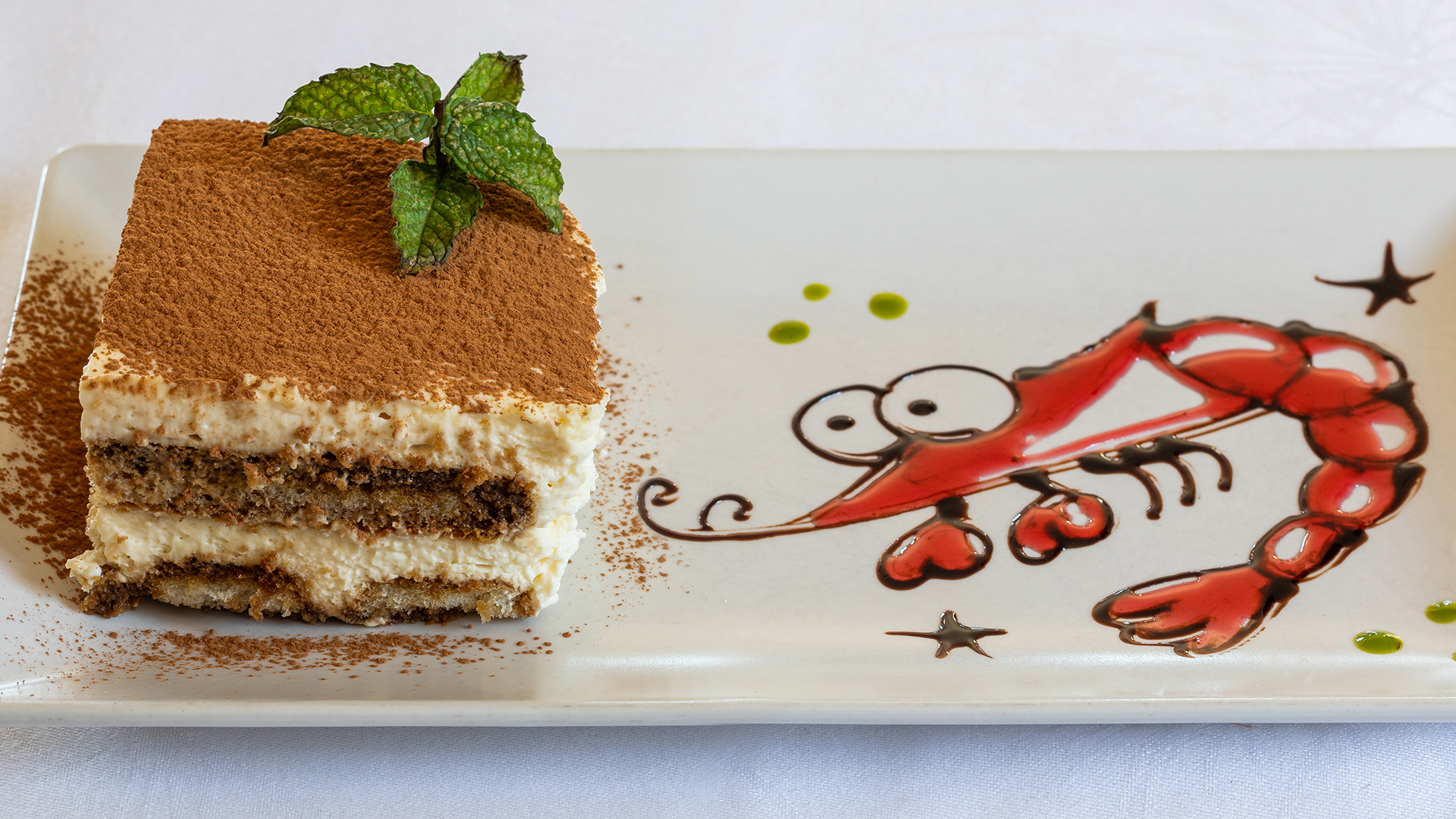 Tiramisu met een met saus getekende garnaal ernaast op het bord bij Can Rafalet