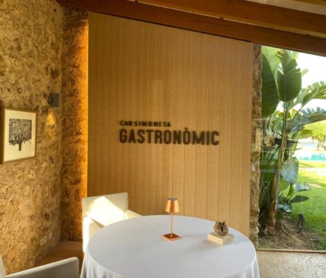 Can Simoneta Gastronòmic (Canyamel): Mexicaans-Mallorcaans menu op de klif 6 De zaal van Can Simoneta Gastronomic met de naam in houten letters op de wand, een ronde gedekte tafel en een natuurstenen muur