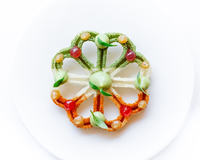 Can Simoneta Gastronòmic (Canyamel): Mexicaans-Mallorcaans menu op de klif 3 Bloemvormig hapje van Can Simoneta met groene en oranje randen, kleine bollen en blaadjes op een wit bord