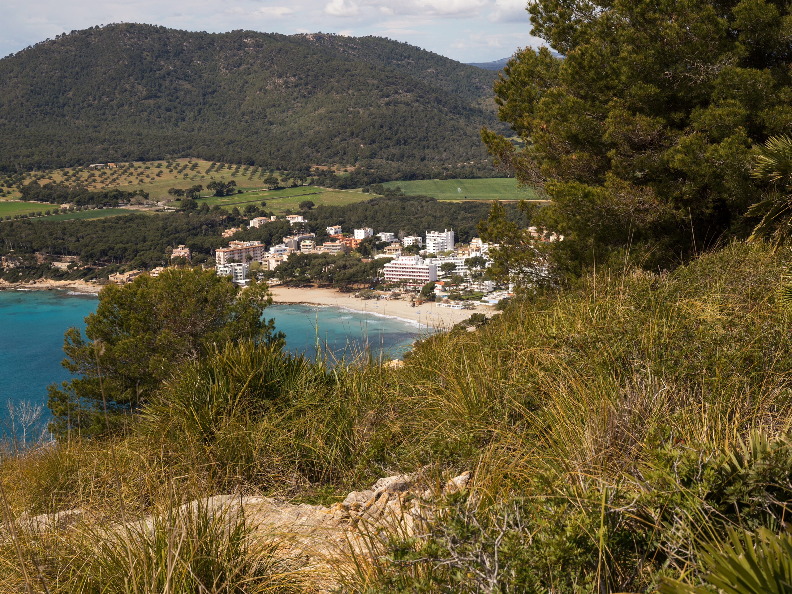 Uitzicht vanaf de hoogte van Cap Vermell op de baai van Canyamel, met het goudkleurige strand, de hotels en de bergen erachter