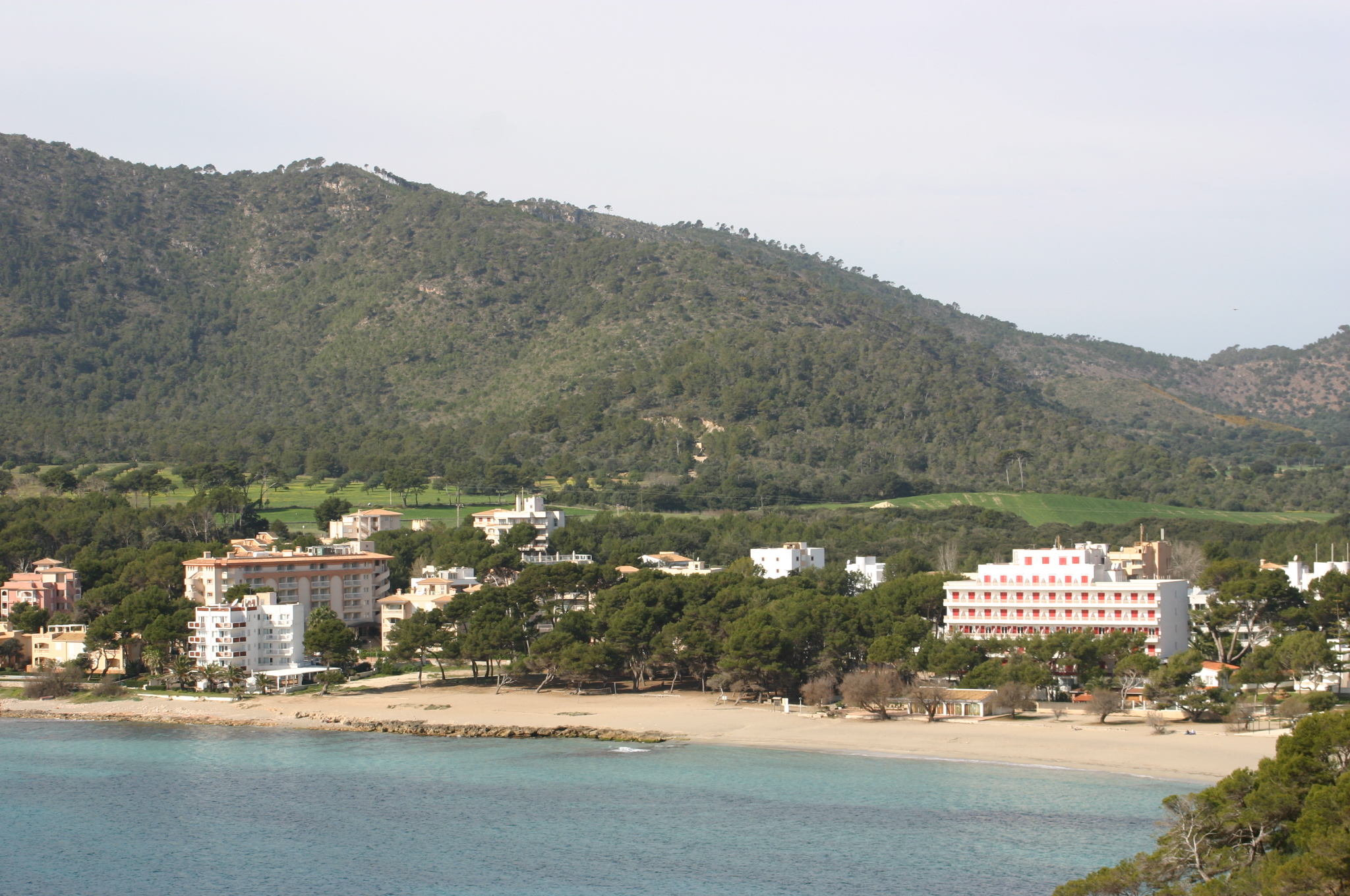 De baai van Canyamel vanaf de zuidkant gezien, met het strand, de witte hotels en de groene heuvels van de Serres de Llevant