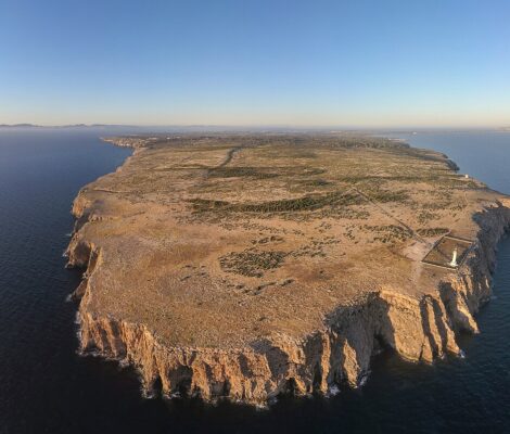Luchtfoto van de hele kaap Cap de Barbaria op Formentera, met de kliffen rondom, de vuurtoren op de rand en Ibiza aan de horizon