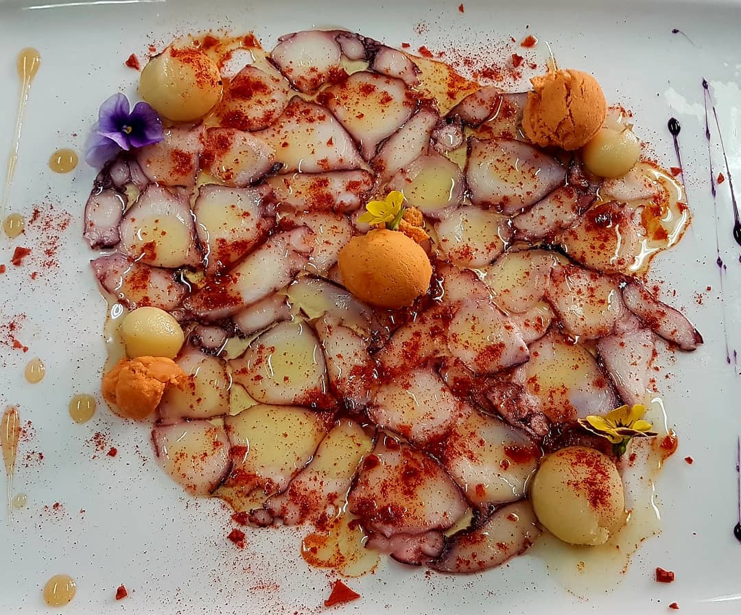 Carpaccio van octopus met pimenton, aardappelbolletjes en viooltjes over een wit bord bij Cas Carreter in Sóller