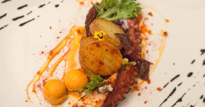 Gegrilde octopus met geroosterde aardappel en eetbare bloemen op een wit bord bij Cas Carreter in Sóller
