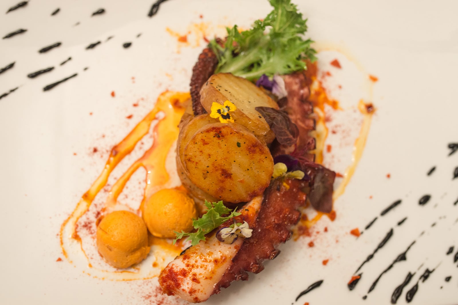 Gegrilde octopus met geroosterde aardappel en eetbare bloemen op een wit bord bij Cas Carreter in Sóller