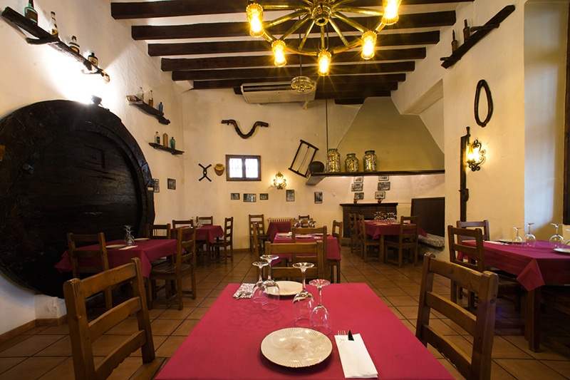 De eetzaal van Cas Carreter in Sóller met rode tafelkleden, houten balken en een groot wijnvat tegen de muur