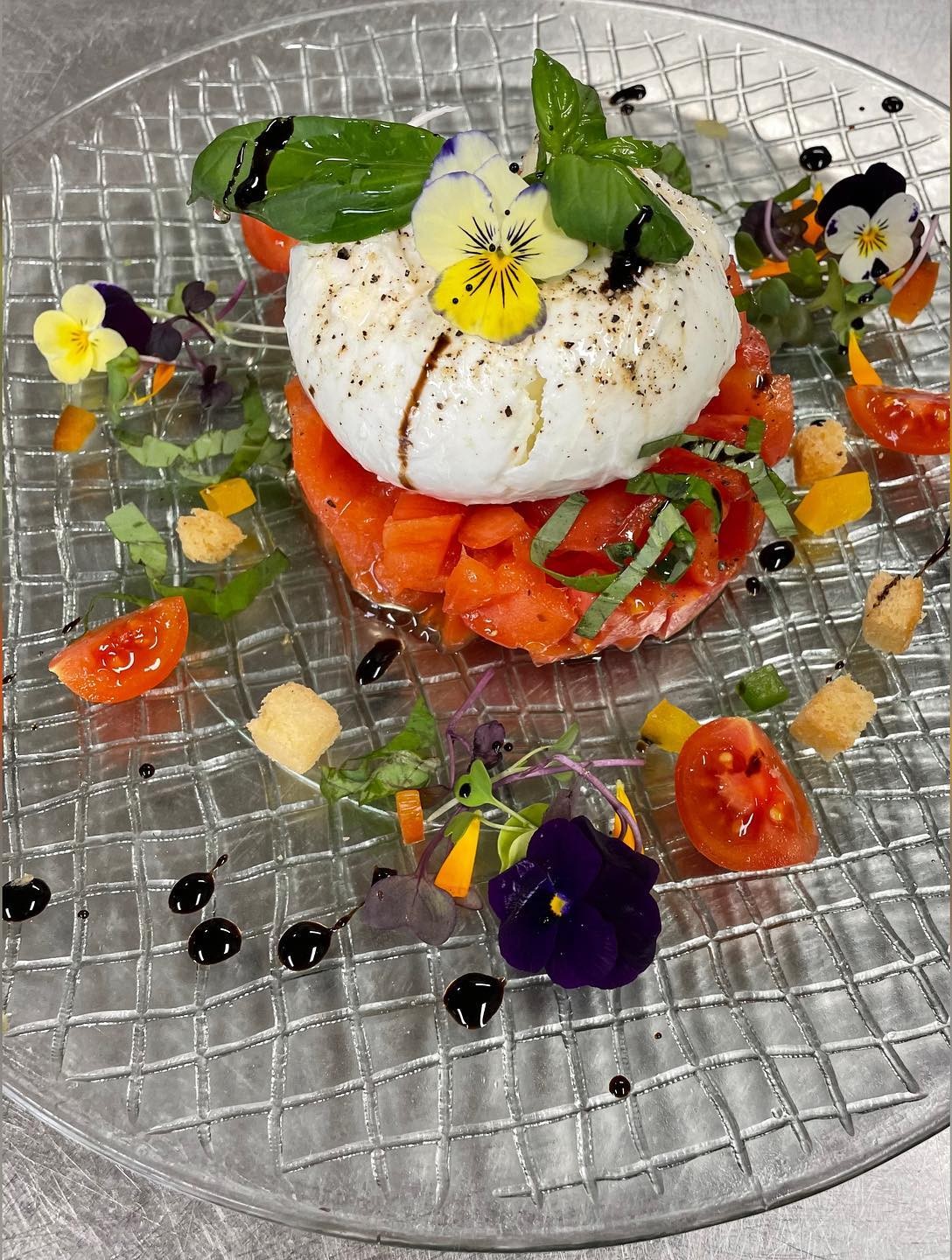 Tomatentartaar met burrata, basilicum en eetbare bloemen op een glazen schaal bij Cas Carreter in Sóller