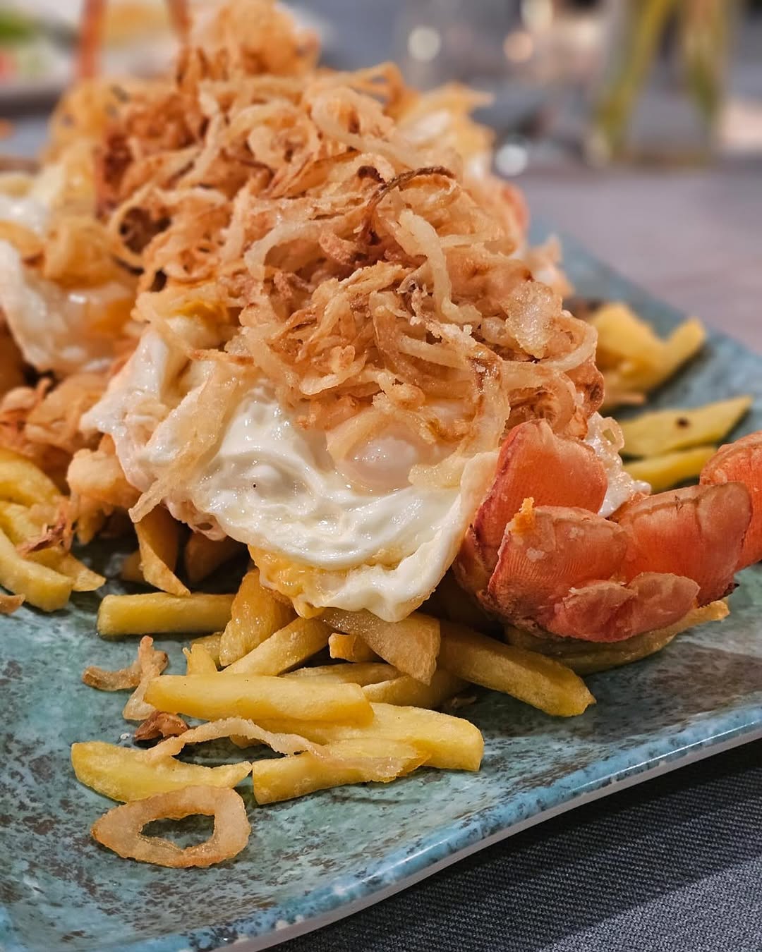 Close-up van langoest met gebakken eieren, friet en een berg goudbruin gefrituurde ui op een turkooizen bord