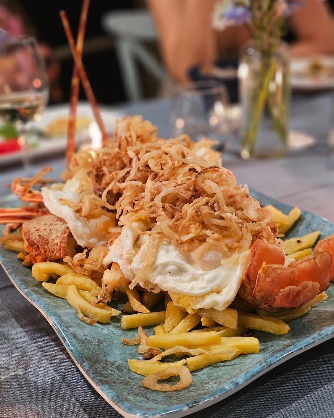 Portie langoest met gebakken ei en friet van Ca's Patró March, gefotografeerd vanaf tafelhoogte met een glas witte wijn op de achtergrond