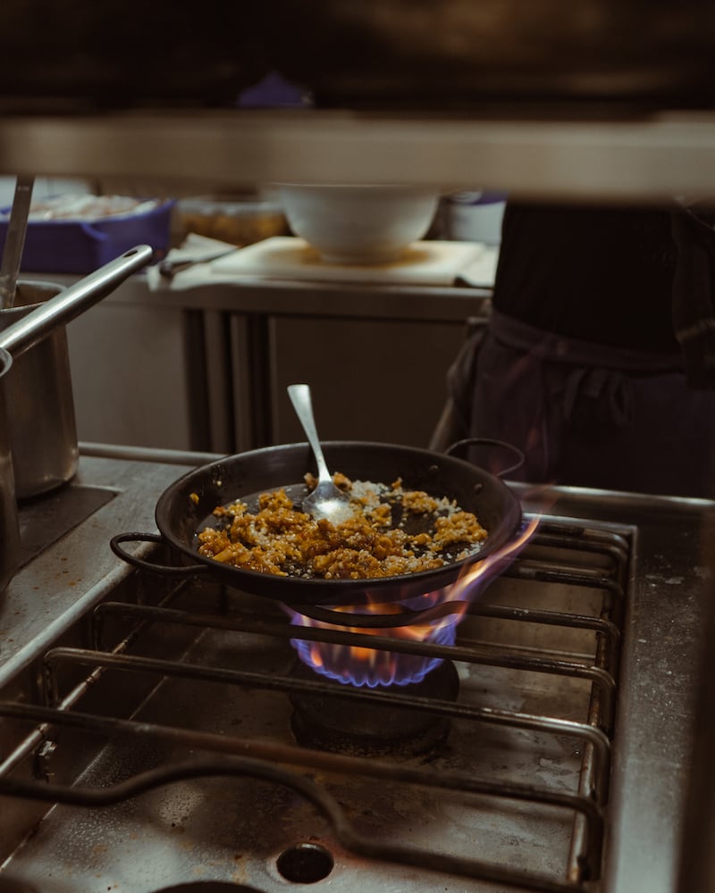 Casa Maruka in Palma: de casa de comidas met een Sol Repsol 2 Een pan rijst met een lepel erin staat op de gasvlam in de keuken van Casa Maruka in Palma