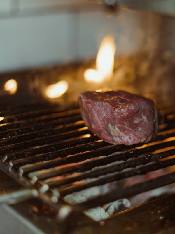 Casa Maruka in Palma: de casa de comidas met een Sol Repsol 3 Een stuk rundvlees ligt boven de vlammen op de houtskoolgrill in de keuken van Casa Maruka in Palma