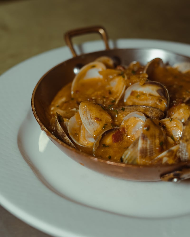 Casa Maruka in Palma: de casa de comidas met een Sol Repsol 4 Koperen pannetje met venusschelpen in een roodbruine saus op een wit bord bij Casa Maruka in Palma