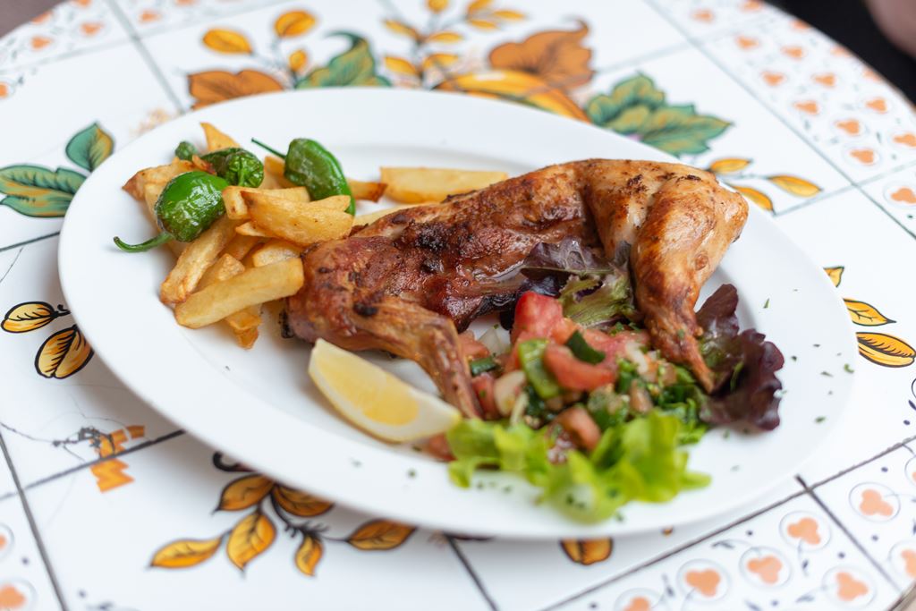 Celler Ca'n Costa in Alcúdia: Mallorquijnse keuken in een huis uit 1594 4 Geroosterd gevogelte met friet, padrónpepers en een frisse salade op een wit bord bij Celler Ca'n Costa in Alcúdia