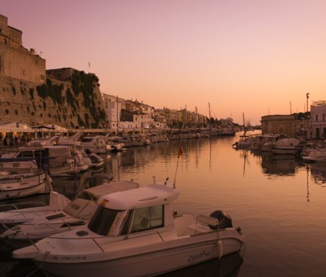 De haven van Ciutadella op Menorca in avondlicht, met de oude stadsmuur en de boten langs de kade