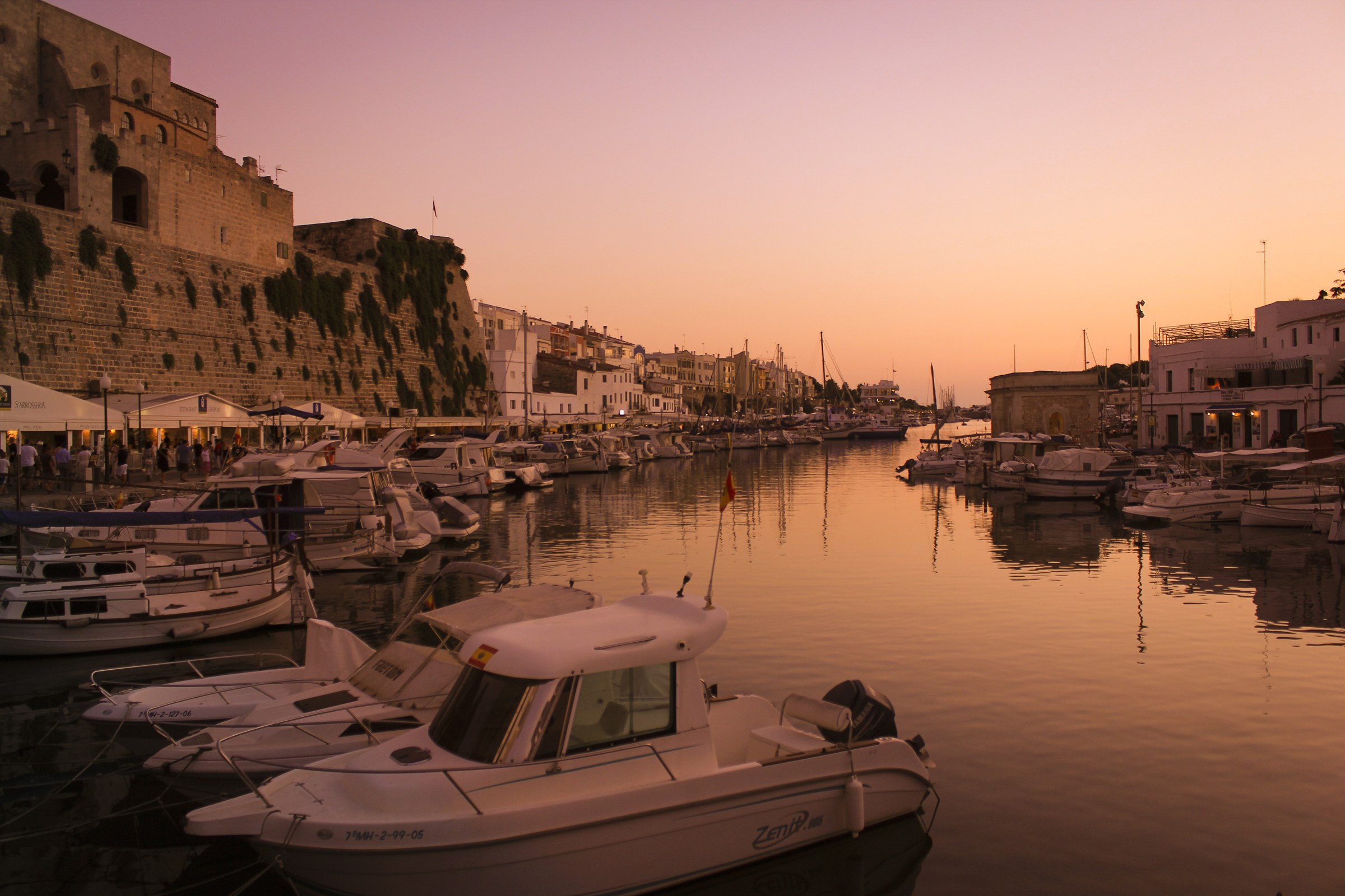 Kopas Club Menorca: drie verdiepingen dansen aan de haven van Ciutadella 1 De haven van Ciutadella op Menorca in avondlicht, met de oude stadsmuur en de boten langs de kade