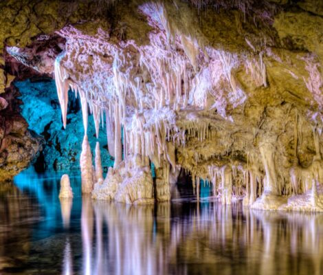 Het ondergrondse meer Mar de Venècia in de Coves dels Hams, met blauw en roze uitgelichte druipsteenformaties die in het stille water weerspiegelen