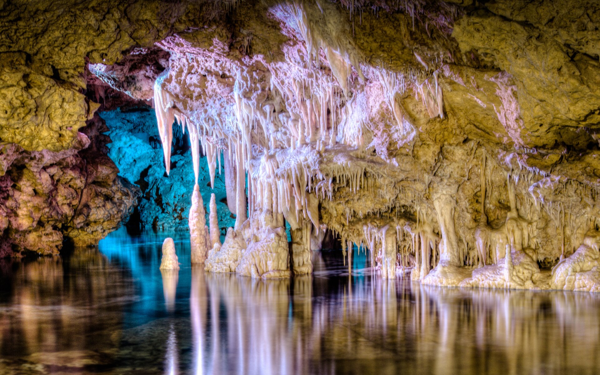 Het ondergrondse meer Mar de Venècia in de Coves dels Hams, met blauw en roze uitgelichte druipsteenformaties die in het stille water weerspiegelen