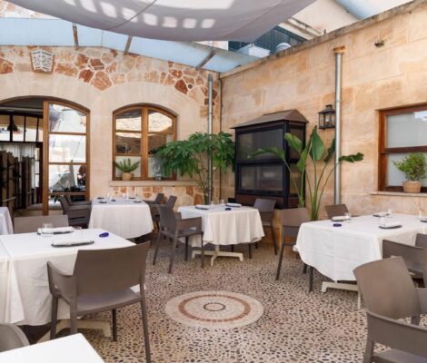 De overdekte binnenplaats van restaurant DaiCa in Llubí met witte tafelkleden, zandstenen muren en een mozaïekvloer