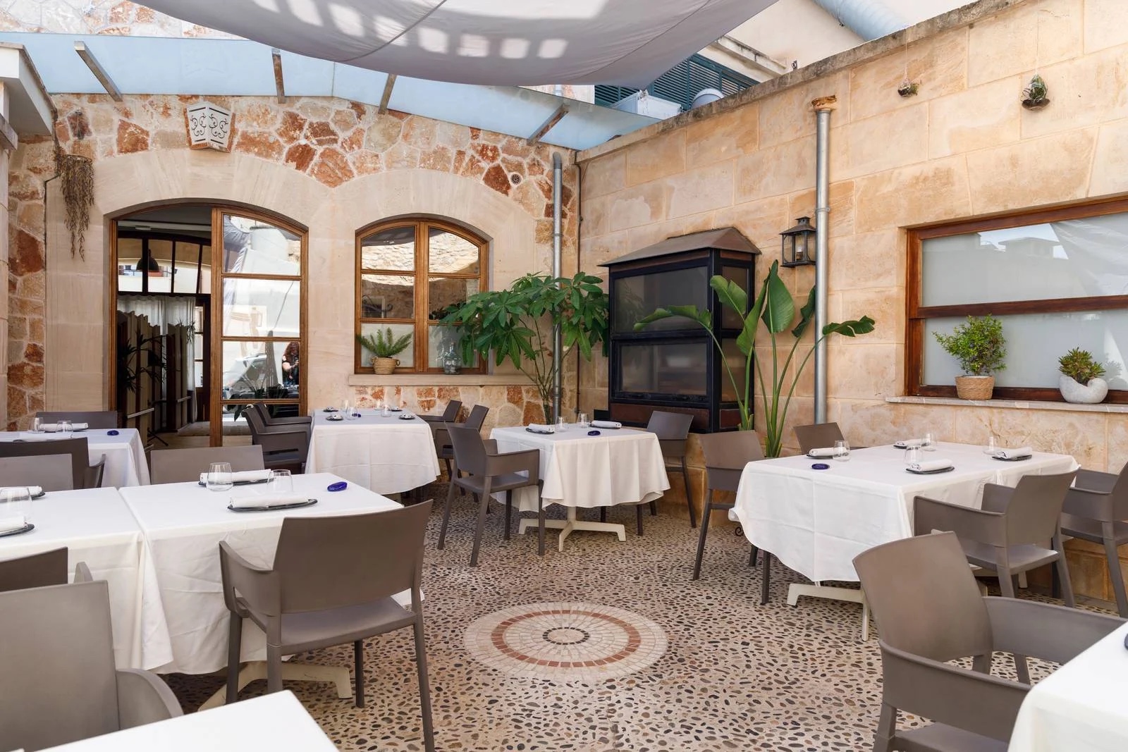 DaiCa in Llubí: dorpsrestaurant met Sol Repsol en drie kamers 1 De overdekte binnenplaats van restaurant DaiCa in Llubí met witte tafelkleden, zandstenen muren en een mozaïekvloer
