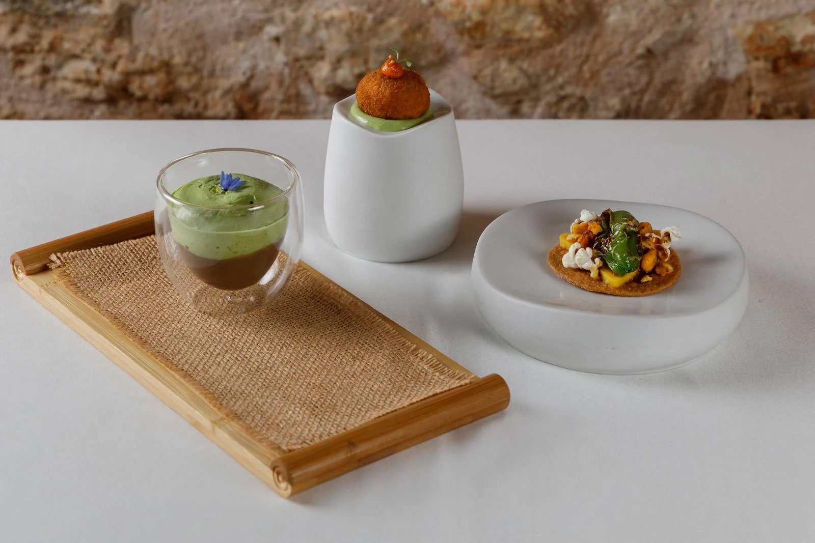 DaiCa in Llubí: dorpsrestaurant met Sol Repsol en drie kamers 6 Drie snacks van DaiCa op wit en bamboe serviesgoed voor een zandstenen muur