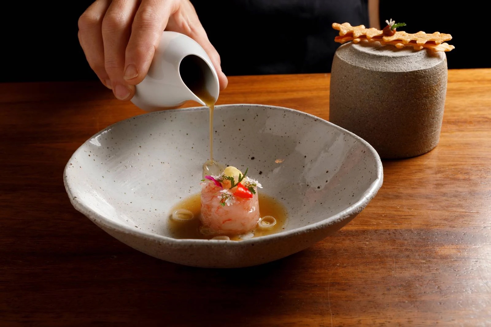 DaiCa in Llubí: dorpsrestaurant met Sol Repsol en drie kamers 7 Bouillon wordt uit een wit kannetje over een rauwe gamba met eetbare bloemen geschonken