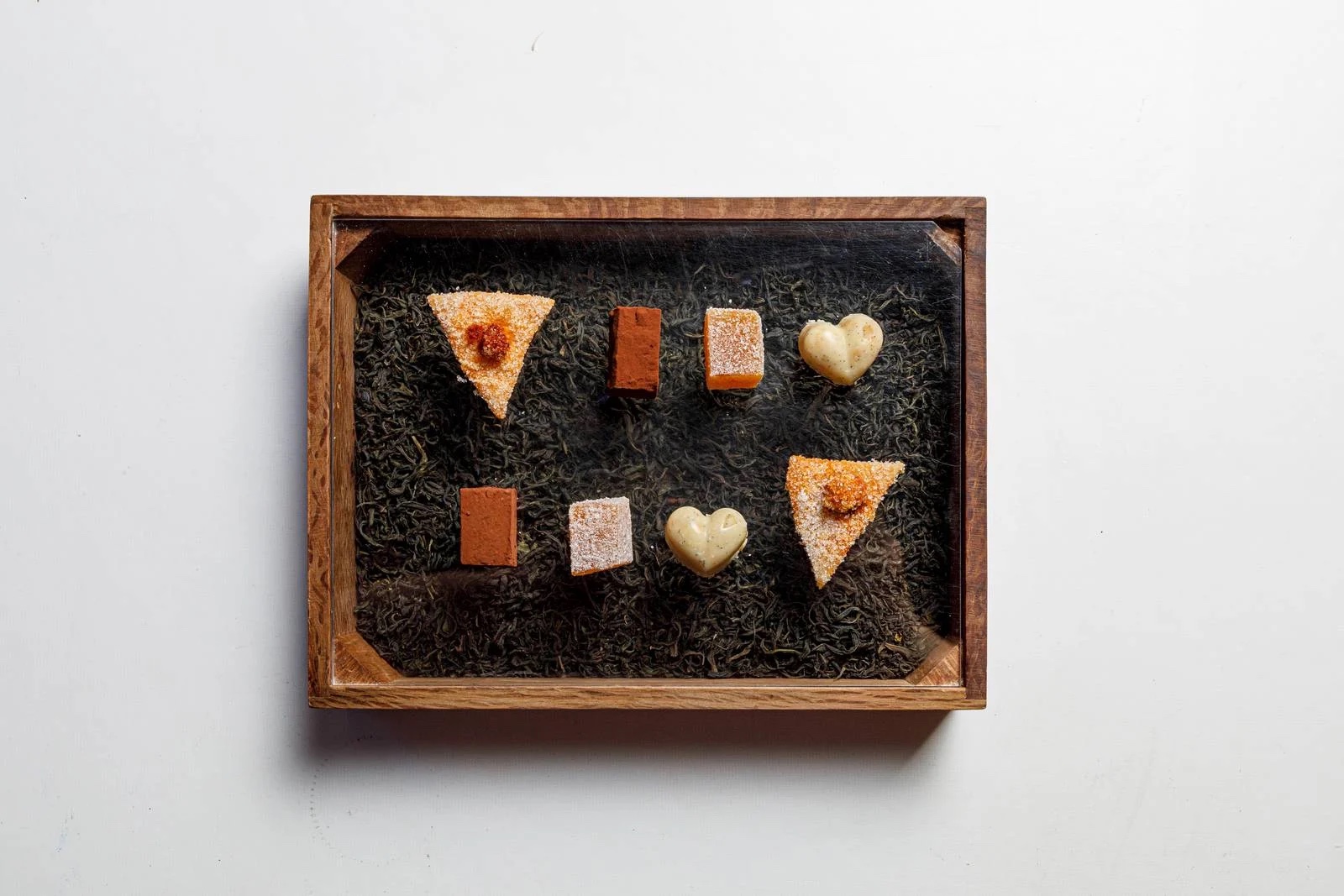 DaiCa in Llubí: dorpsrestaurant met Sol Repsol en drie kamers 8 Petitfours van DaiCa in een houten bakje op een bedje van losse theeblaadjes