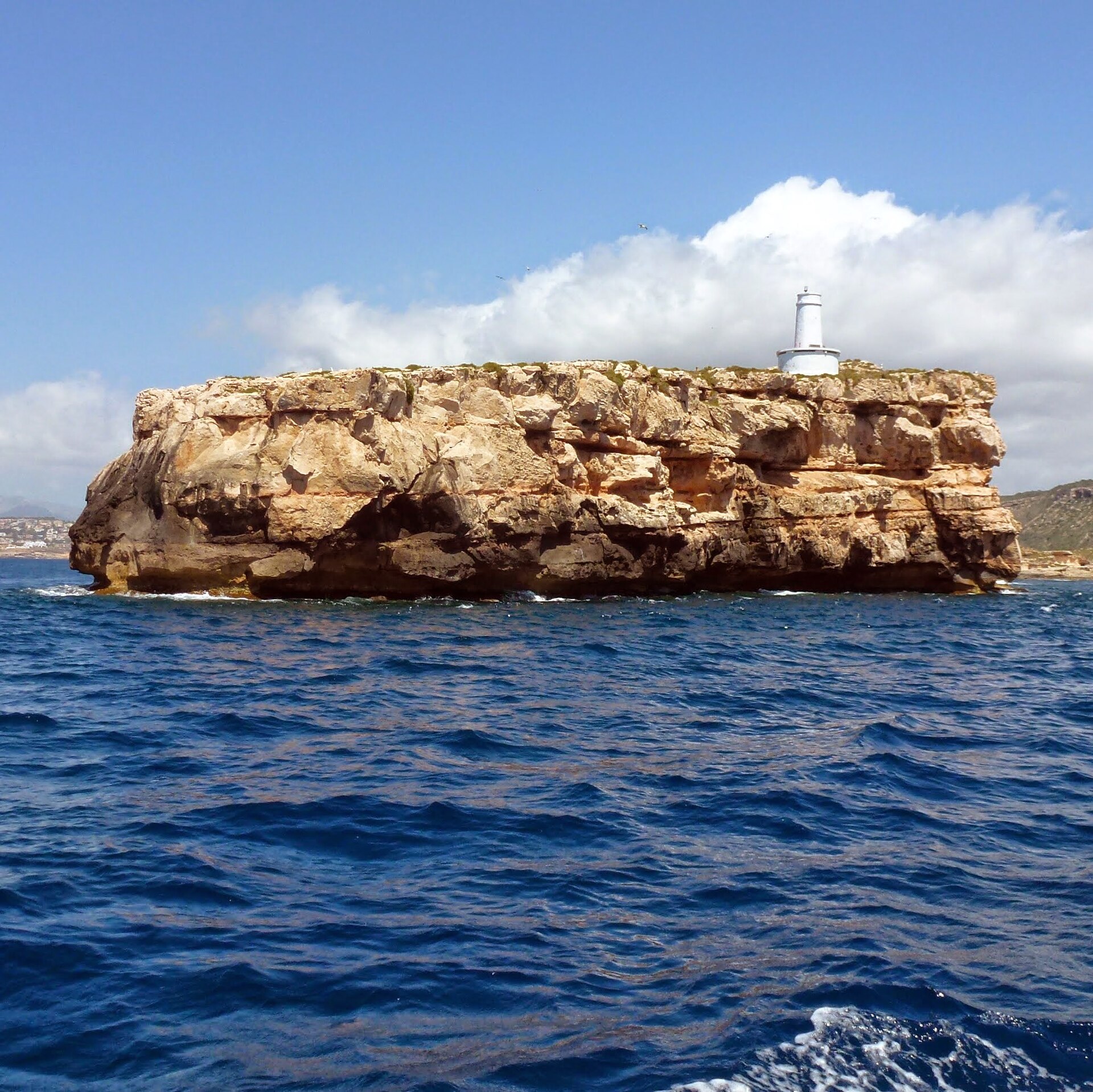 Het vlakke rotseiland Illa del Toro met zijn witte vuurtoren, voor de zuidwestkust van Mallorca