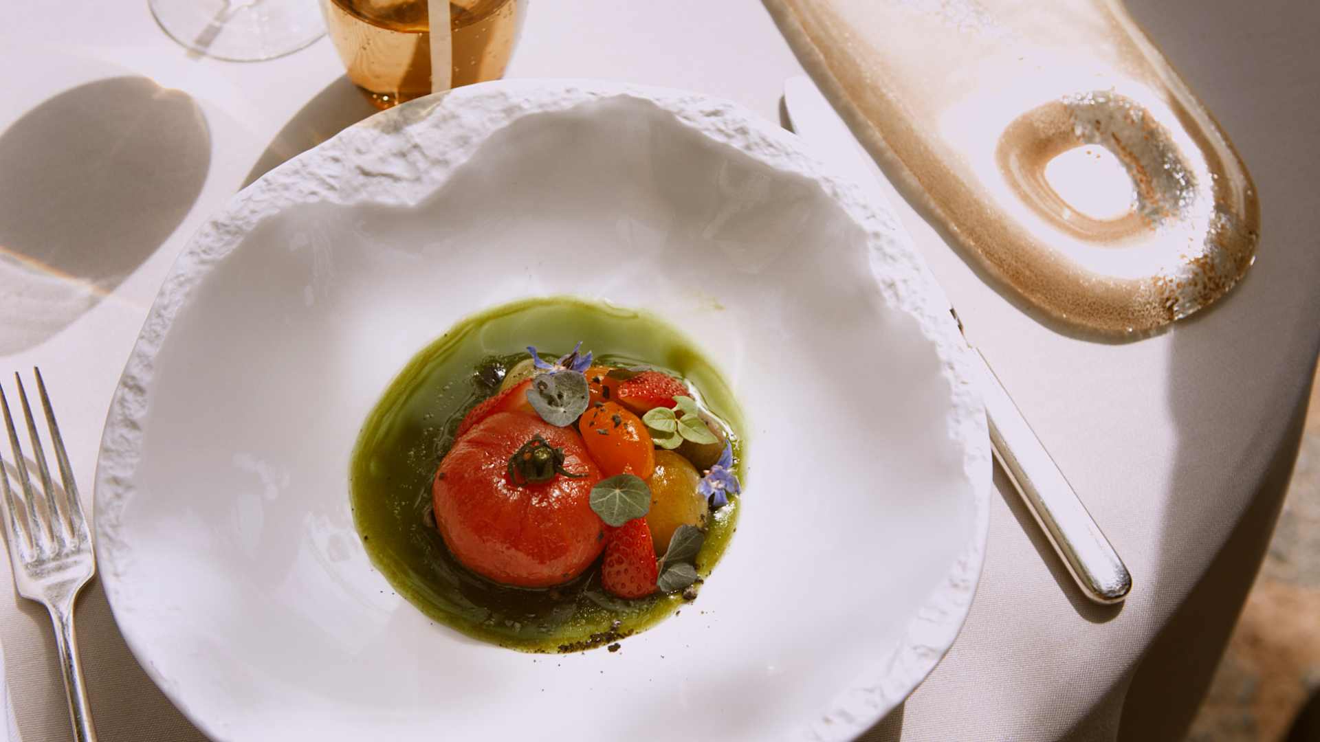 Gerecht van El Olivo in Deia met een gepelde ramallet-tomaat, aardbei en kruiden in een groene olie op een wit bord