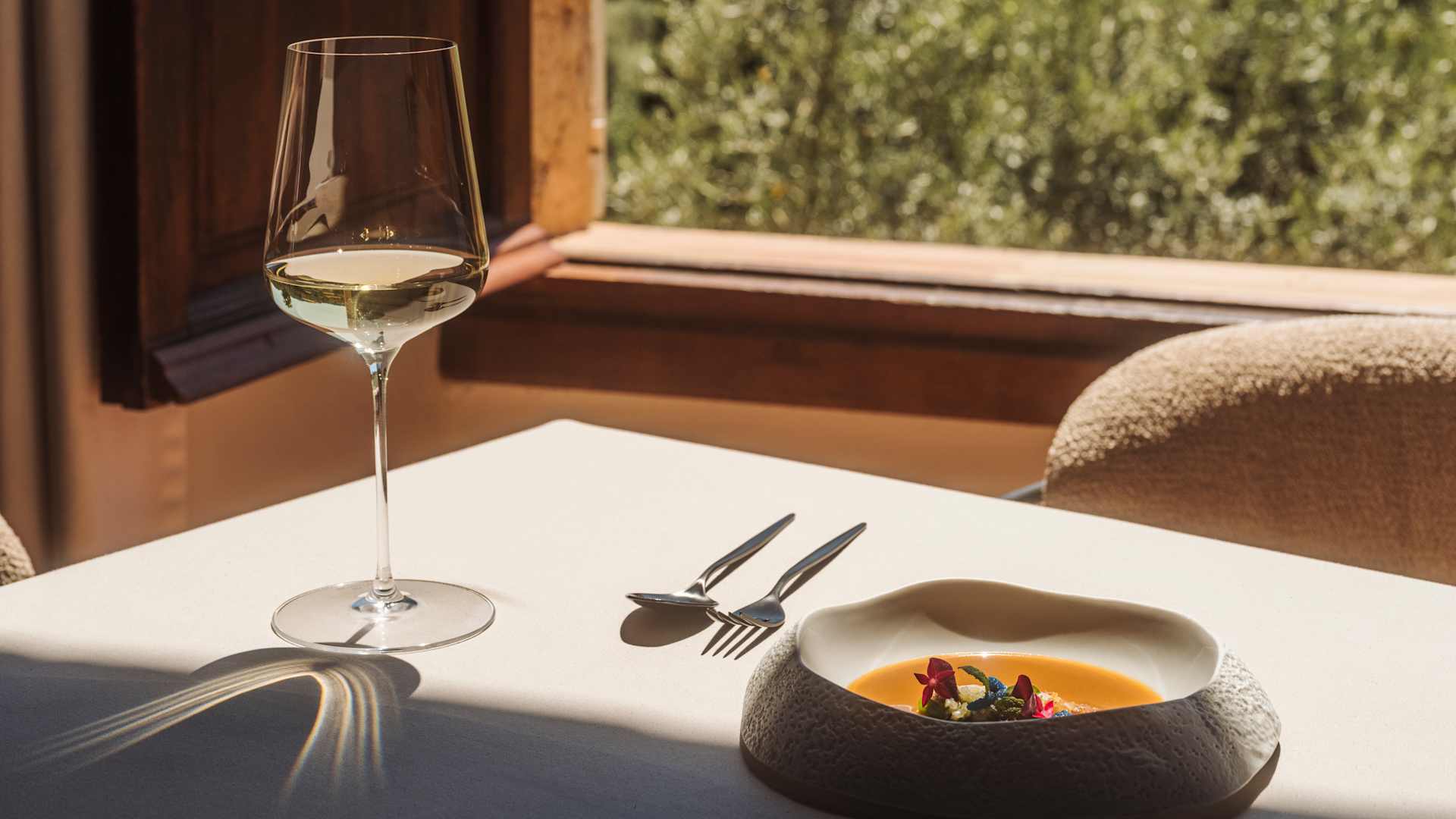 Gerecht in een stenen schaal met een glas witte wijn op een tafel bij het open venster van El Olivo