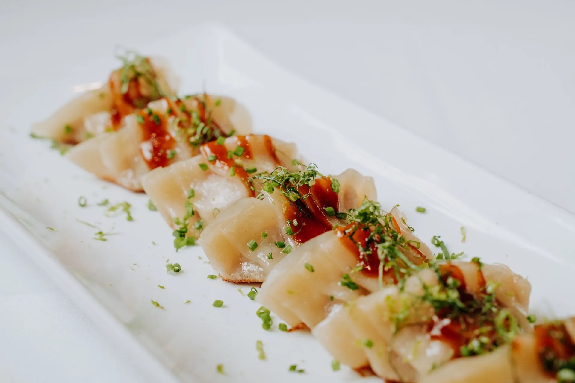 Emilio Innobar in Palma: fine fusion van Japan, Mexico en Mallorca 2 Dun gesneden rauwe vis op een langwerpig wit bord bij Emilio Innobar in Palma, afgemaakt met tomaat, bieslook en limoenrasp