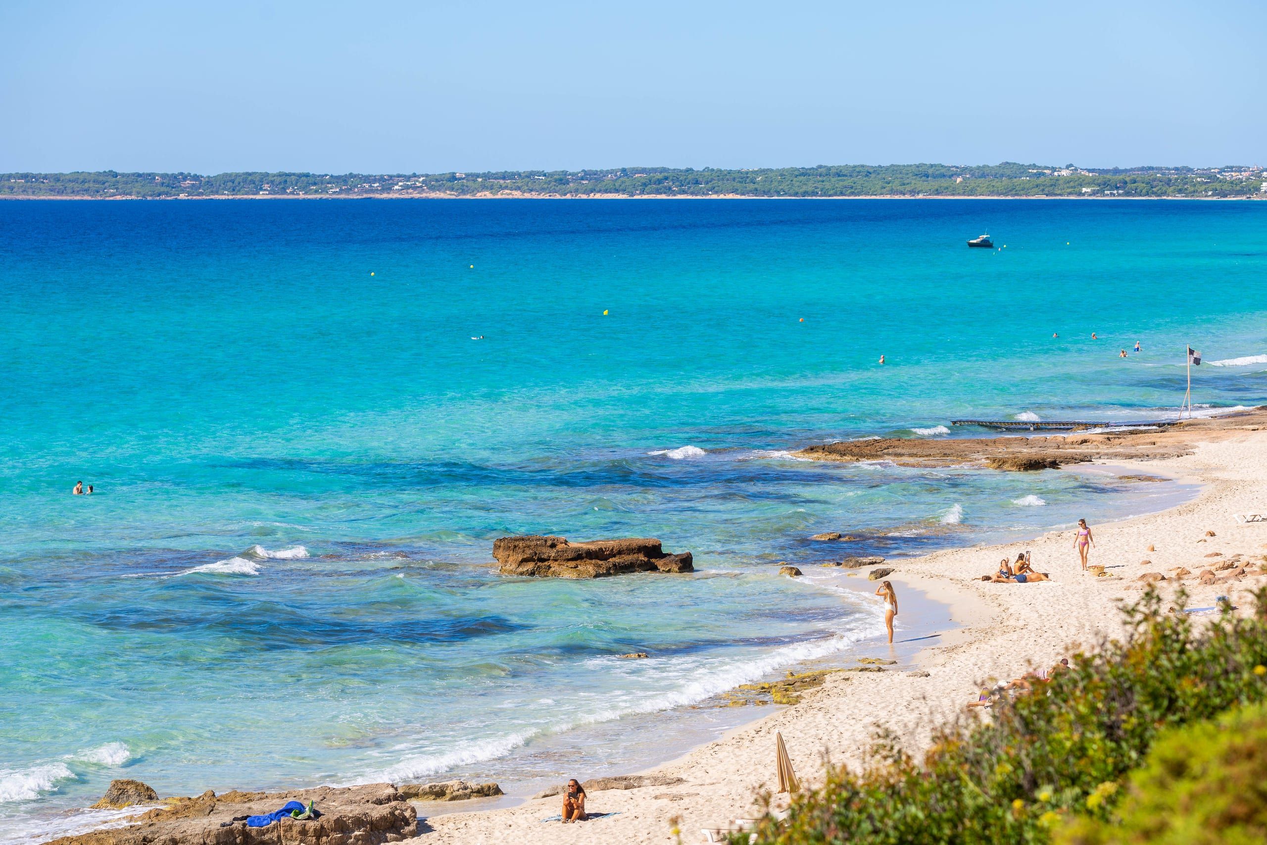 Es Arenals Formentera: het best uitgeruste deel van Migjorn 1 Het brede lichte zand van Es Arenals op Formentera met turquoise water, rotsplaten aan de waterlijn en badgasten op het strand
