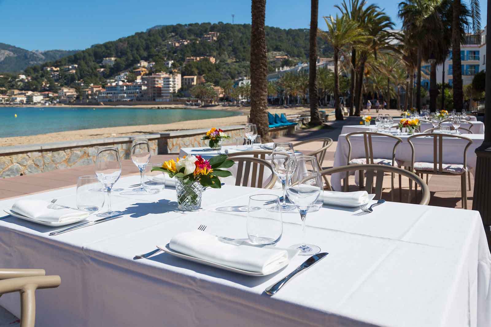 Een gedekte tafel op het terras van Es Canyís aan de boulevard, met palmen en de baai van Port de Sóller erachter