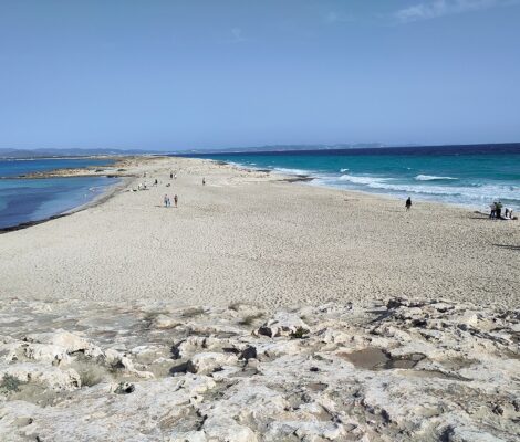 De zandlandtong van Es Trucadors op Formentera met rustig water links en branding rechts, en Ibiza aan de horizon
