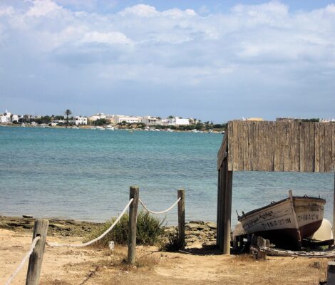 De lagune Estany des Peix op Formentera met een houten botenhuis, een opgetrokken vissersboot en La Savina aan de overkant