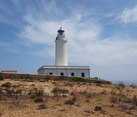 De witte vuurtoren Far de la Mola op Formentera met het wachtershuis, op het kale plateau met de zee rechts