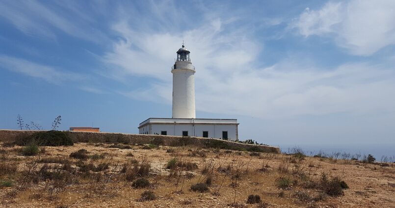 De witte vuurtoren Far de la Mola op Formentera met het wachtershuis, op het kale plateau met de zee rechts