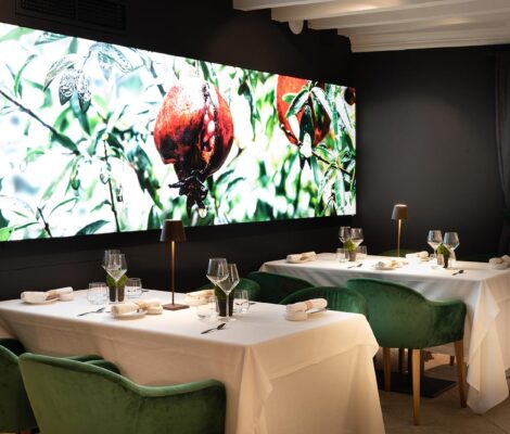 De eetzaal van restaurant Fera in Palma met witte tafellakens, groene fluwelen stoelen en een verlichte wandfoto van granaatappels aan de boom