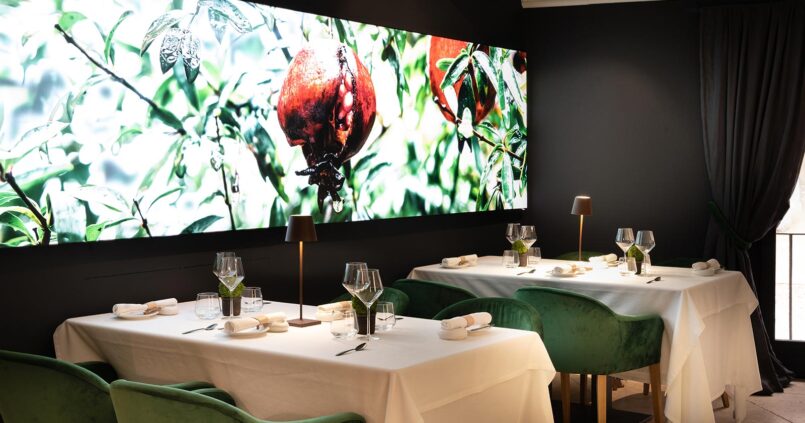 De eetzaal van restaurant Fera in Palma met witte tafellakens, groene fluwelen stoelen en een verlichte wandfoto van granaatappels aan de boom