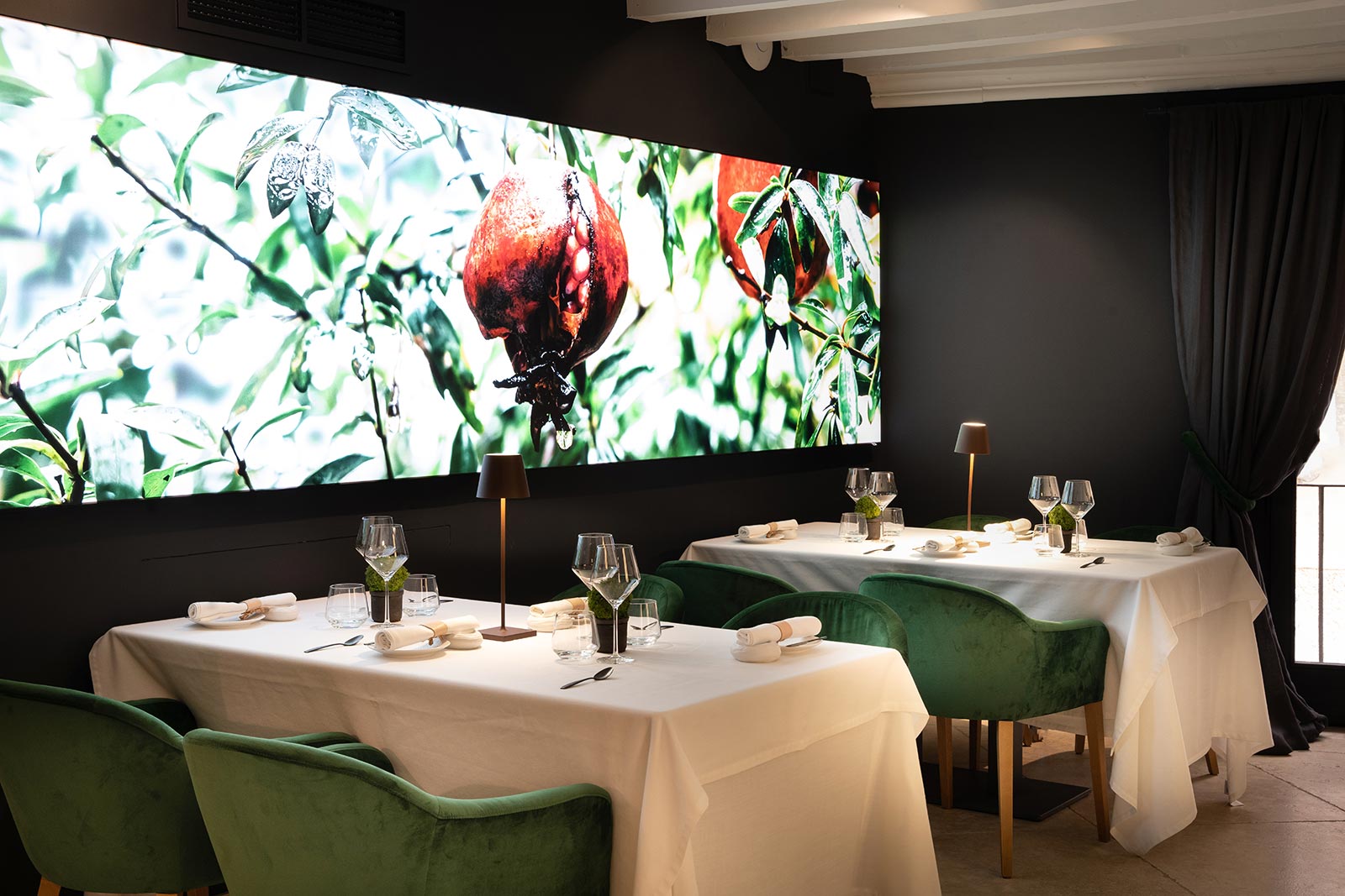 De eetzaal van restaurant Fera in Palma met witte tafellakens, groene fluwelen stoelen en een verlichte wandfoto van granaatappels aan de boom