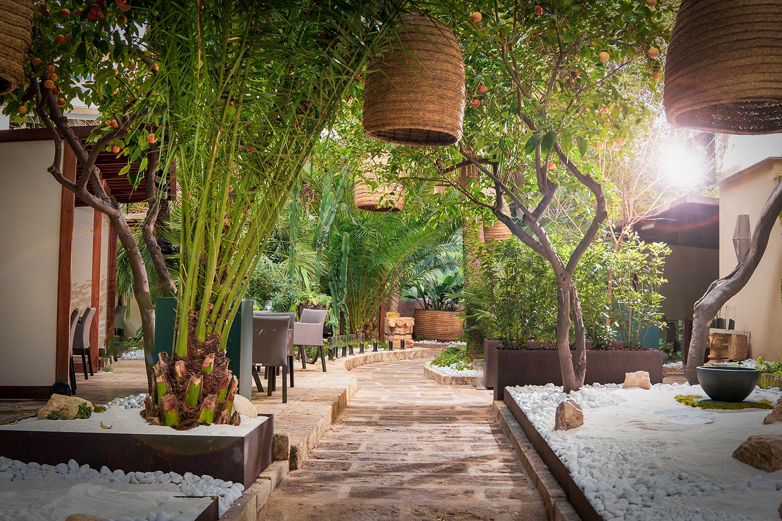 De binnentuin van Fera in Palma met dadelpalmen, sinaasappelbomen, wit grind en hangende lampen van touw boven een natuurstenen pad