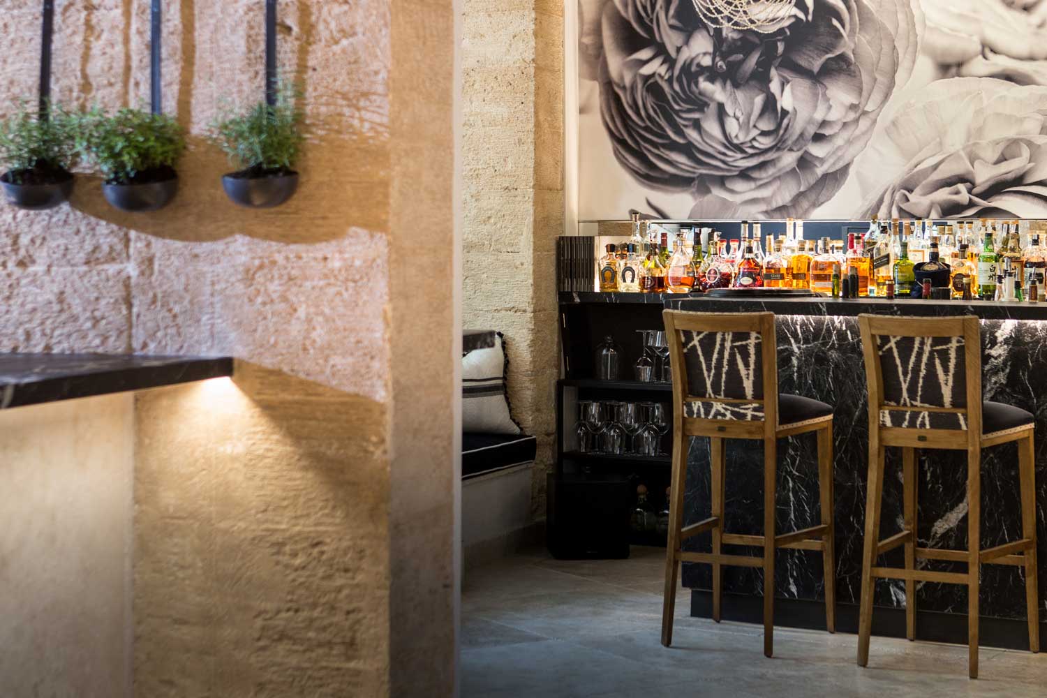 De bar van Fera in Palma met een zwartmarmeren toog, houten krukken en potjes kruiden aan een ruwe zandstenen muur