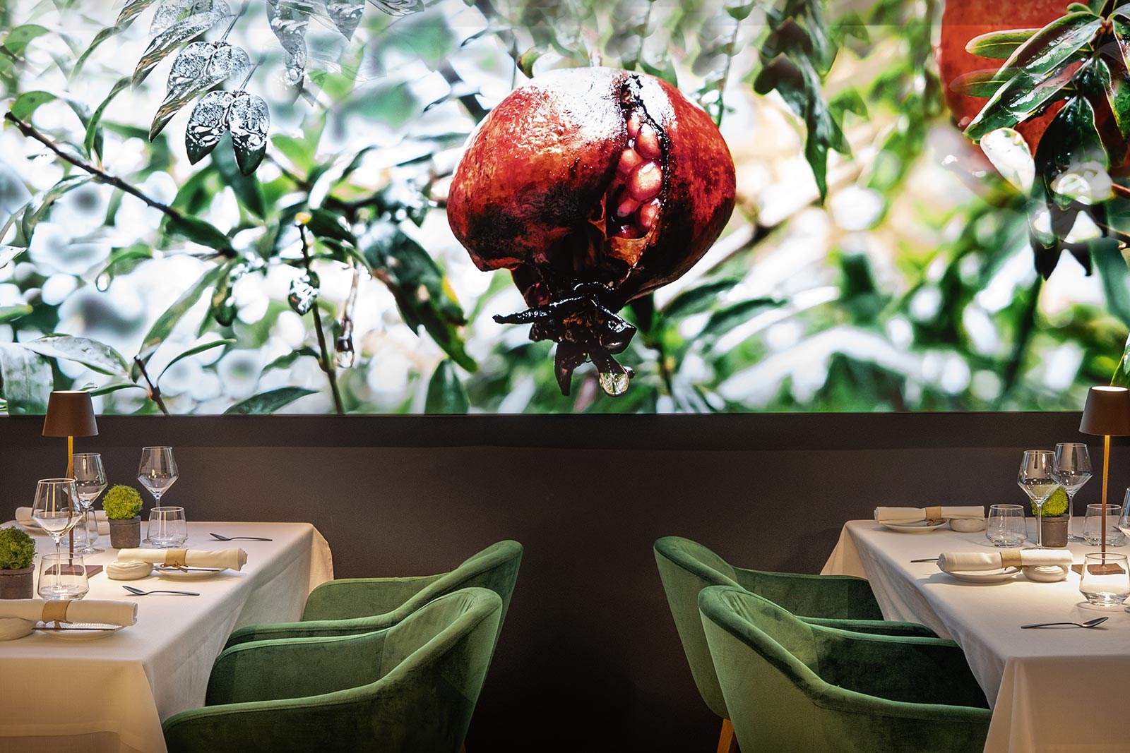 Twee gedekte tafels met groene fluwelen stoelen voor de verlichte wandfoto van granaatappels in de eetzaal van Fera in Palma
