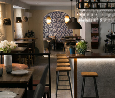 De smalle eetzaal van restaurant Fervor in Palma met houten tafels, een bar met krukken en een gewelfde doorgang met blauw bladerbehang