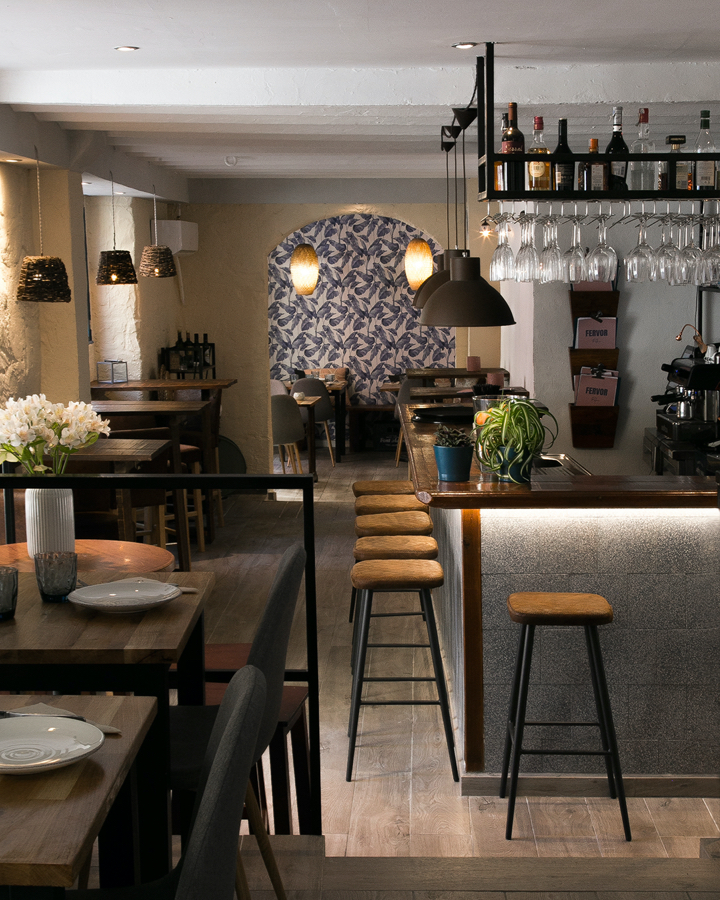 Fervor Palma: eten in een oude kantine uit 1890 1 De smalle eetzaal van restaurant Fervor in Palma met houten tafels, een bar met krukken en een gewelfde doorgang met blauw bladerbehang