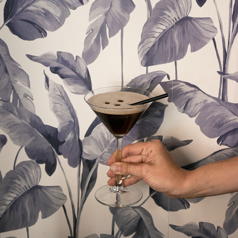 Fervor Palma: eten in een oude kantine uit 1890 7 Donkere cocktail met schuimlaag in een glas op voet, voor de bladerbehangen wand van Fervor in Palma